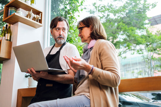 Cafe owner and business advisor discussing marketing or finance using smart phones. Both are smiling and engaged, symbolizing teamwork, strategy, and modern small business collaboration. - Powered by Adobe