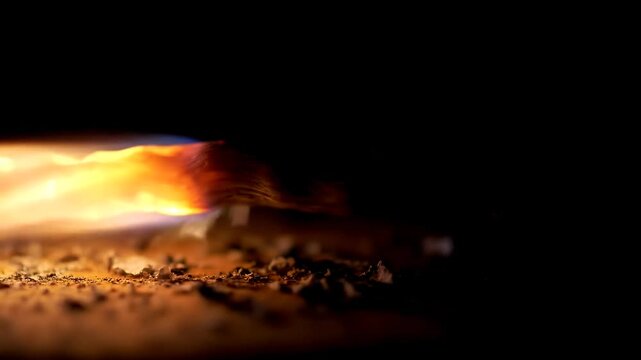 Extreme close-up of a burning fuse igniting a trail of gunpowder on a dark background in slow motion
