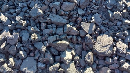 A close-up view of a pile of gray gravel and small rocks, showcasing natural textures and irregular shapes under bright sunlight
