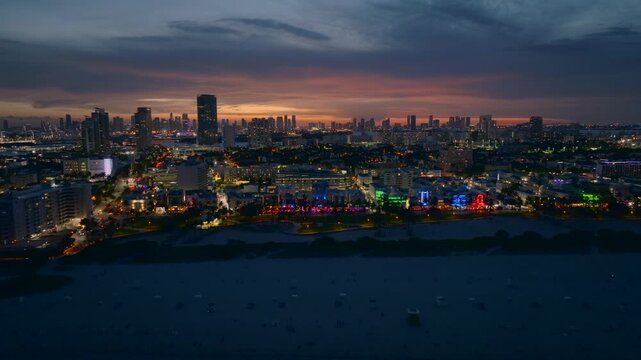 Aerial view of Ocean Drive buildings glowing with vivid colors against the darkening twilight sky near the beach, Miami Beach, Florida, United States.