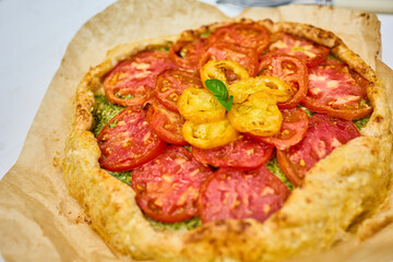 A delicious tomato galette is displayed on parchment paper, showcasing layers of vibrant red and yellow tomatoes atop a flaky crust in a warm kitchen atmosphere.