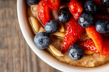 Oatmeal with ripe strawberries, blueberries and honey in the bowl. Selective focus.