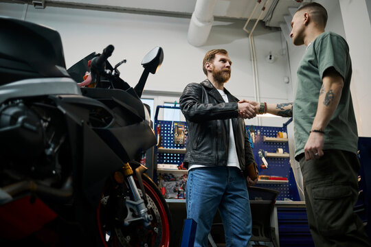 Client and specialist shaking hands in motorcycle workshop