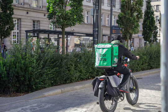 Poznan, Poland - July 16, 2025: Uber Eats delivery rider with green thermal bag on bicycle, cycling a city street, symbolizing modern food delivery