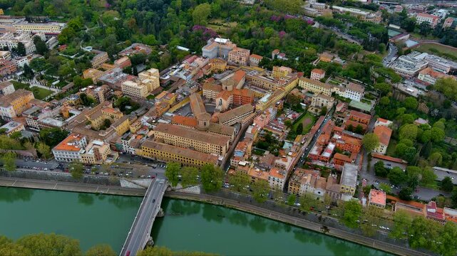 Dramatic drone shot over Rome&rsquo;s leafy Trastevere district: the historic San Michele complex enclosed by terracotta lanes, a busy Ponte Sublicio crossing the emerald Tiber and green Janiculum slopes.
