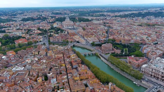 Sweeping drone panorama of Rome highlighting St Peter&rsquo;s Basilica, Castel Sant&rsquo;Angelo and Ponte Sant&rsquo;Angelo along the Tiber River, framed by terracotta rooftops and distant Lazio hills in Italy.