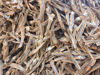 A detailed shot of numerous dried anchovies stacked together, showcasing texture and natural detail, captured in a market setting. Perfect for food, culinary, or traditional market-related purposes.