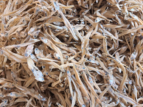A detailed shot of numerous dried anchovies stacked together, showcasing texture and natural detail, captured in a market setting. Perfect for food, culinary, or traditional market-related purposes.