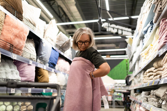 Mature woman shopping for home textiles in a large home improvement store, exploring various options and assessing quality