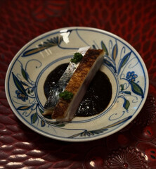 Grilled mackerel plated with dark savory sauce.