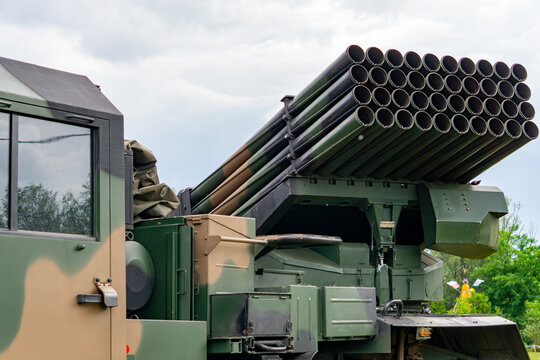 Multiple rocket launcher mounted on a military vehicle with camouflage. Side view with sky and trees in the background