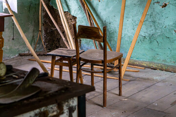Old chairs in an abandoned, decaying room with a green wall and scattered wooden planks. Atmosphere of neglect.