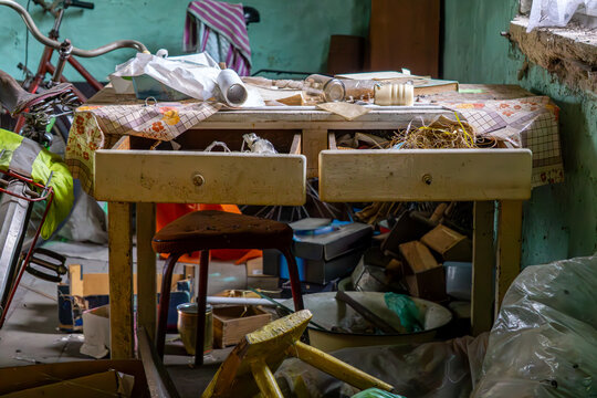 Cluttered table in an abandoned room, filled with old items and tools. A bicycle and green wall in the background.