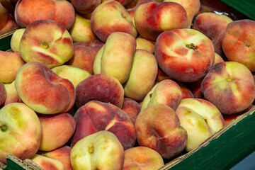 Juicy flat peaches (Saturn peaches) arranged in a crate at a market. Colorful, ripe fruits with a distinctive flattened shape.