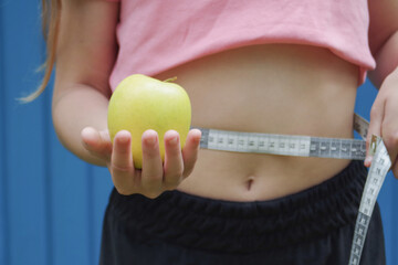 a girl with a measuring tape around her waist holds an apple in her hand