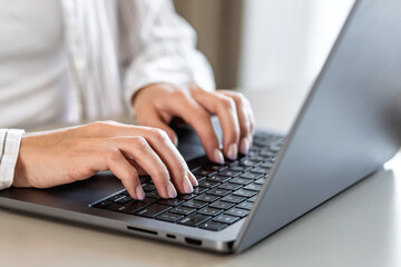 Close-up of woman's hands typing on laptop keyboard, working remotely or studying online indoor