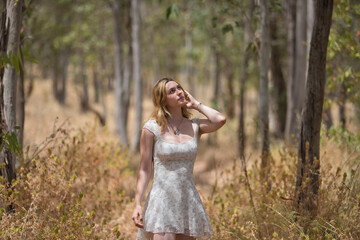 Young woman, beautiful, blonde, wearing a floral dress, relaxed and calm, walking among the trees, in connection with nature and ecology, in an outdoor park. Concept of beauty, youth, millennial.