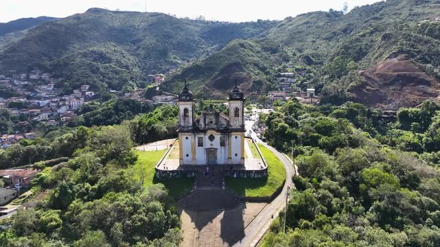 drone pulling back from the Church of S&atilde;o Francisco de Paula in Ouro Preto Brazil revealing its complete baroque architecture and the surrounding mountainous landscape of this UNESCO site