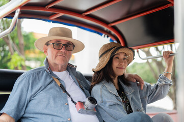 Couple of old white man and asian woman sitting riding in tuk tuk or three wheel taxi touring a city