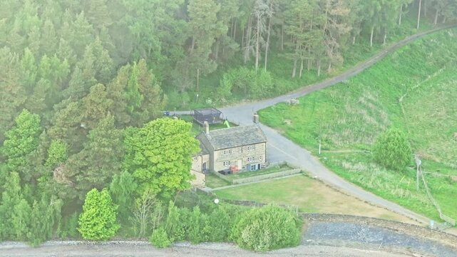Aerial: house near Strines Reservoir, water storage reservoir, with forest during the day near Sheffield, South Yorkshire, England, crane down drone shot