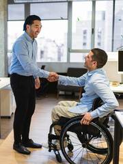 Two happy businessmen shaking hands, one of them using a wheelchair, in a modern coworking office....