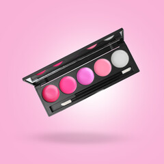 Lip palette with brush in air against pink background. Makeup cosmetics