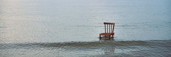 Wooden chair stands in calm, vast ocean, symbolizing solitude and contemplation. Stillness of water...