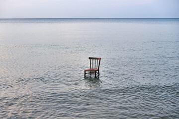 Single wooden chair stands in tranquil sea at dusk, evoking solitude and contemplation. Serene...