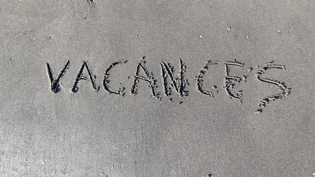 Le mot "Vacances" &eacute;crit dans le sable et happ&eacute; par les vagues