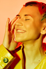 smiling woman with colorful red hair and yellow jacket enjoying bright studio light, closed eyes,...