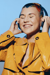 joyful woman with colorful hair enjoys music in large headphones, wearing a bright yellow leather...