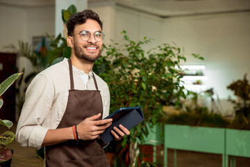 Fototapeta premium Male flower shop assistant standing with a tablet in hands