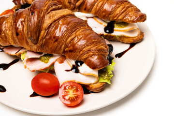 Two freshly baked classic delicious fresh organic croissants with ham, cheese, pesto sauce and tomatoes on a white ceramic plate isolated on white background