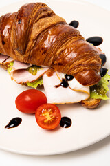Freshly baked classic delicious fresh organic croissant with ham, cheese, pesto and tomatoes on white ceramic plate isolated on white background