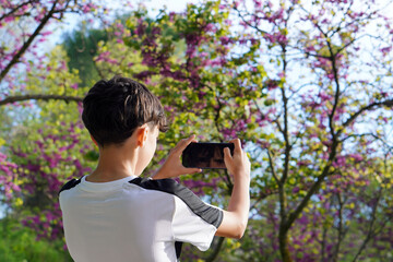 Happy Teenage Boy on His Back Taking Pictures with Mobile Phone in Nature