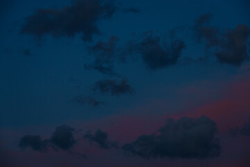 Scattered dark clouds float across a twilight sky bathed in deep blue and delicate pink tones, creating a peaceful and moody scene with copy space.