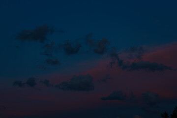Scattered dark clouds float across a twilight sky bathed in deep blue and delicate pink tones,...