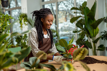 Smiling young woman with dreadlocks plating flowers and looking involved