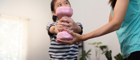 Mother assisting daughter with a pink dumbbell workout at home