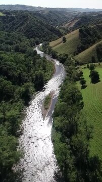 A Breathtaking Aerial Drone Shot Flying Over a Winding River as it Flows Through a Lush Green Valley with Rolling Hills, Ideal for Travel Documentaries