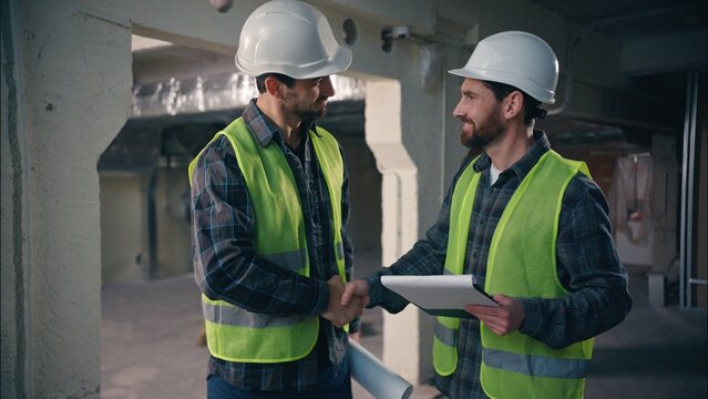 Glad Caucasian workers men guys holding draft papers mechanics working project architects plan build manufacture males engineers discuss construction in factory builders teamwork cooperation handshake