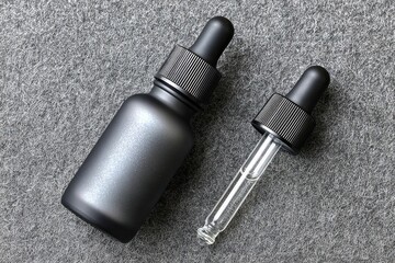 Naklejka premium Two dark gray, matte-finish dropper bottles on a gray textured surface