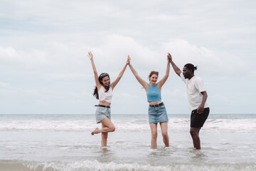 Group of diverse young friends enjoying fun time at the beach, raising hands and laughing together in ocean water. Concept of friendship, travel, freedom, and summer holiday joy.