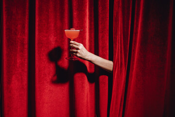 Hand holding a cocktail glass in front of a red curtain