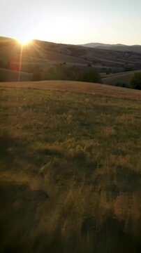 A Fast-Paced FPV Drone Flight Skimming Low Over Rolling Green Hills at Sunset, with a Bright Lens Flare, Ideal for Dynamic and Action-Packed Videos