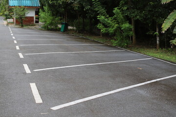 Open-air parking lot with multiple white cars under a bright sky, surrounded by tropical trees and buildings in the background.