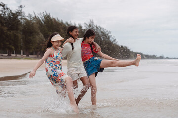 Obraz premium Asian and multicultural friends walking and splashing in beach water, enjoying childhood freedom, friendship, and outdoor fun in a playful and joyful summer moment.