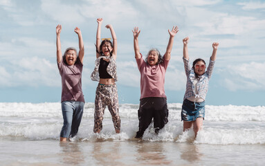Asian multi generational family enjoying joyful moments on the beach. Happy women and daughter splashing water together, fun, bonding, and freedom across ages.