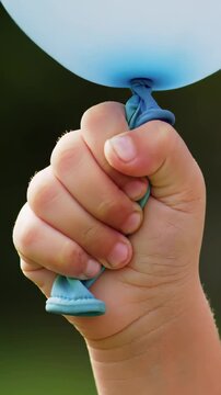 A Close-Up Shot of a Small Child's Hand Tightly Gripping a Blue Balloon Outdoors, Symbolizing Childhood Innocence and Joy, Ideal for Family-themed Content