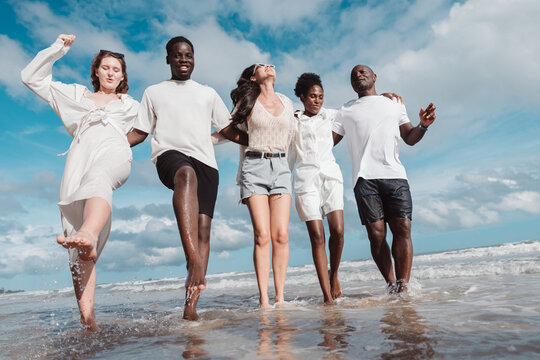 Happy diverse group of friends together on the beach, Active friendship, summer fun, positivity, and joyful lifestyle by the sea.